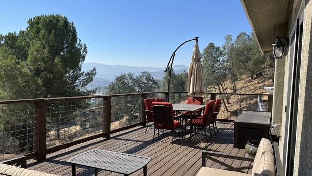 Une terrasse dotée de mobilier d’extérieur, d’une table et de chaises, offrant une vue imprenable sur un paysage pittoresque, avec des arbres et des collines.