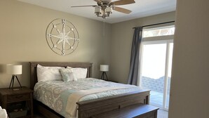 Une chambre à coucher avec un lit en bois, des lampes de chevet, un ventilateur de plafond, un décor mural représentant une boussole et une grande fenêtre avec des rideaux.