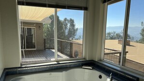 Une salle de bain dotée d’une grande baignoire, donnant sur une terrasse, et comprenant une fenêtre avec des stores.