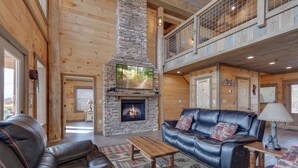 A spacious living room with a stone fireplace, leather furniture, and a wooden ceiling. - Great Smoky Lodge by Jackson Mountain Rentals (Gatlinburg)