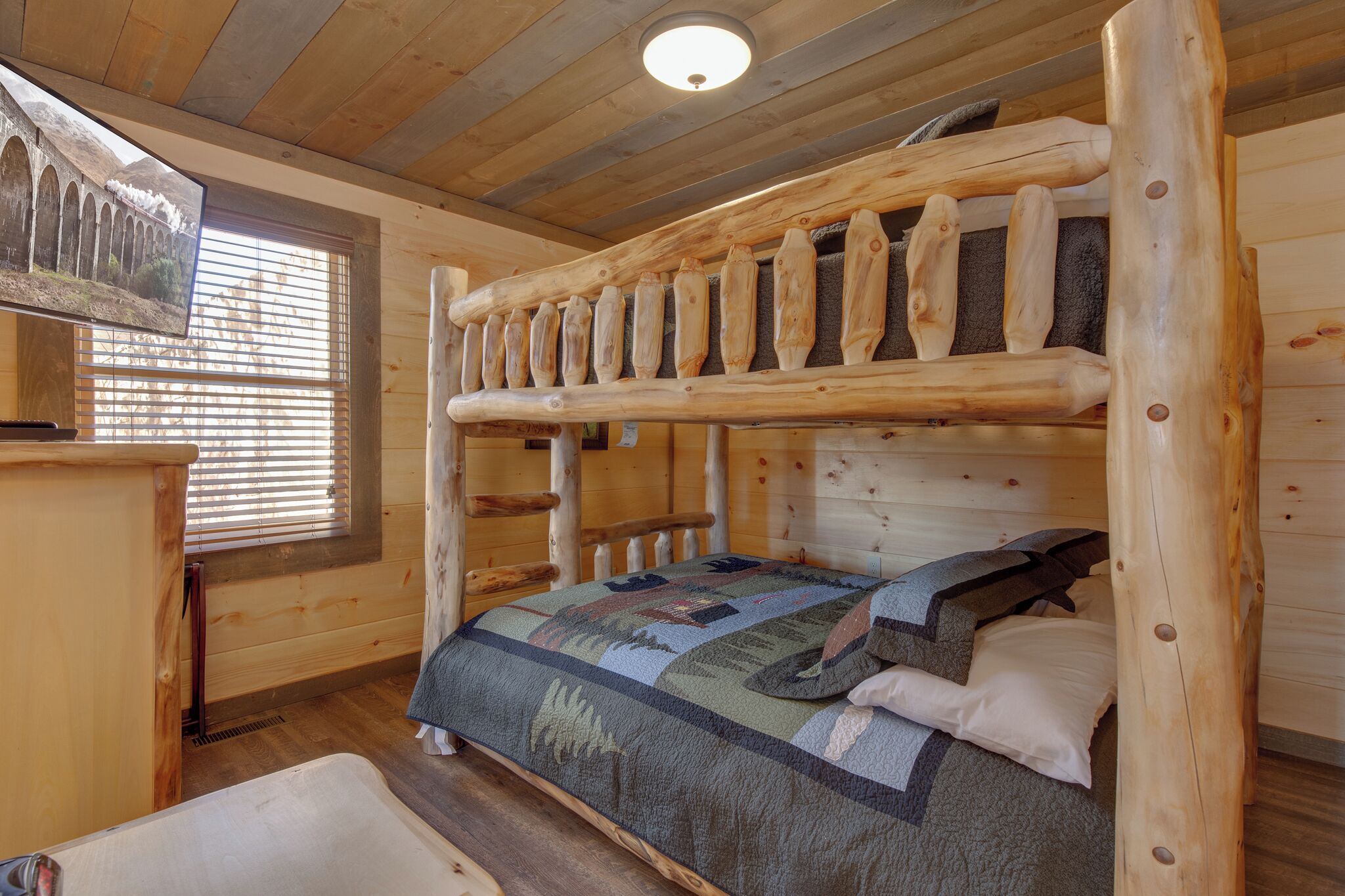 Una habitación tipo cabaña de madera con literas, un aparador de madera y una ventana con persianas.