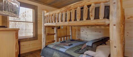 A wooden cabin room with bunk beds, a wooden dresser, and a window with blinds.