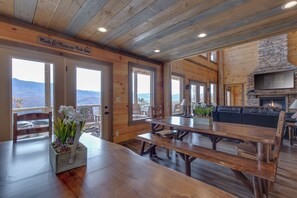 A wooden interior with a dining area, a stone fireplace, and a view of the mountains.