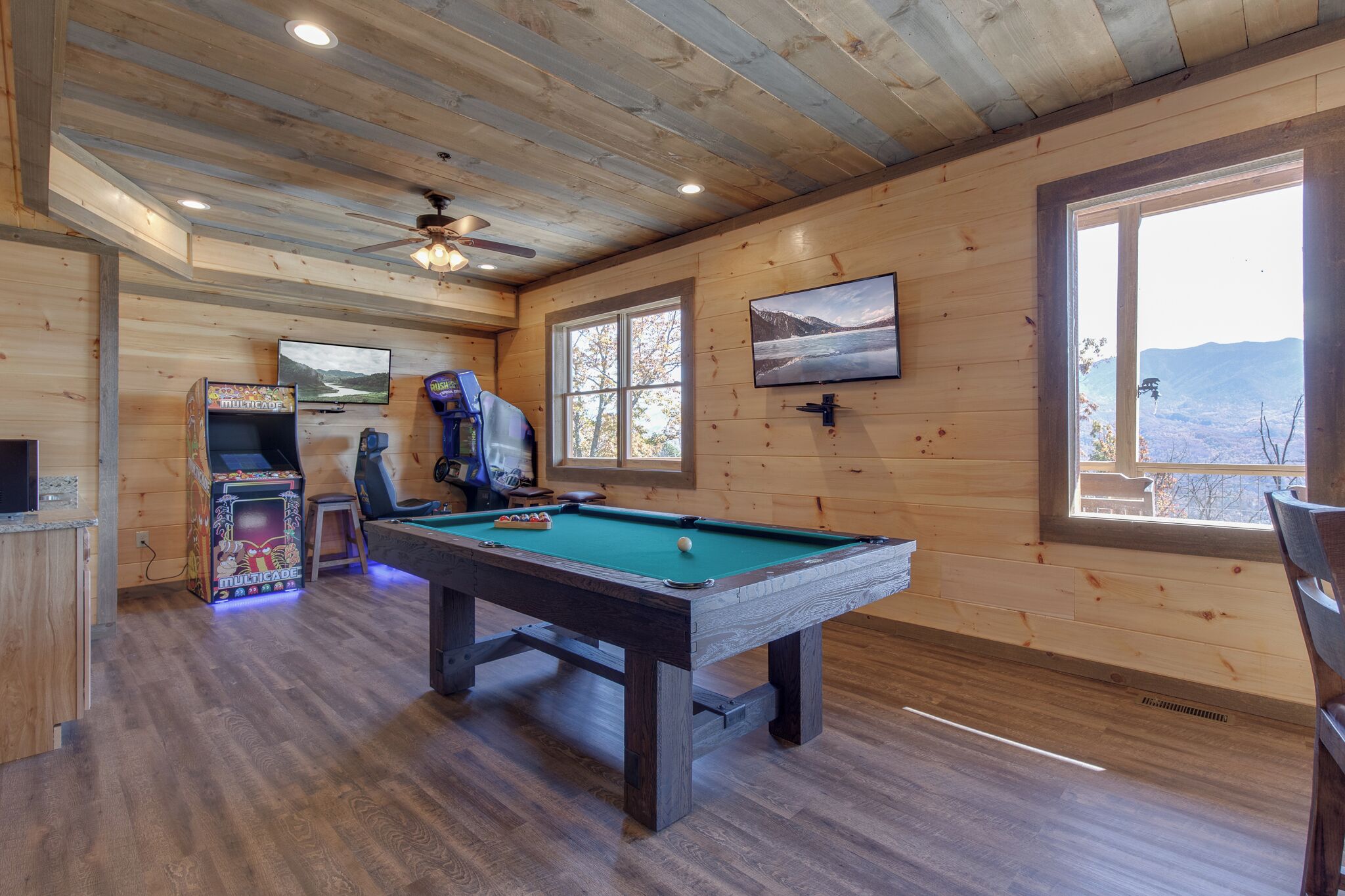 A wooden interior with a pool table, a television, and a view of the mountains.