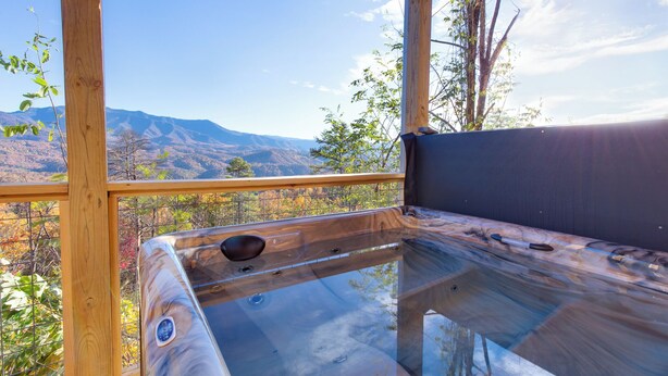 A wooden deck with a glass table and bench, offering a view of mountains. - Great Smoky Lodge by Jackson Mountain Rentals (Gatlinburg)