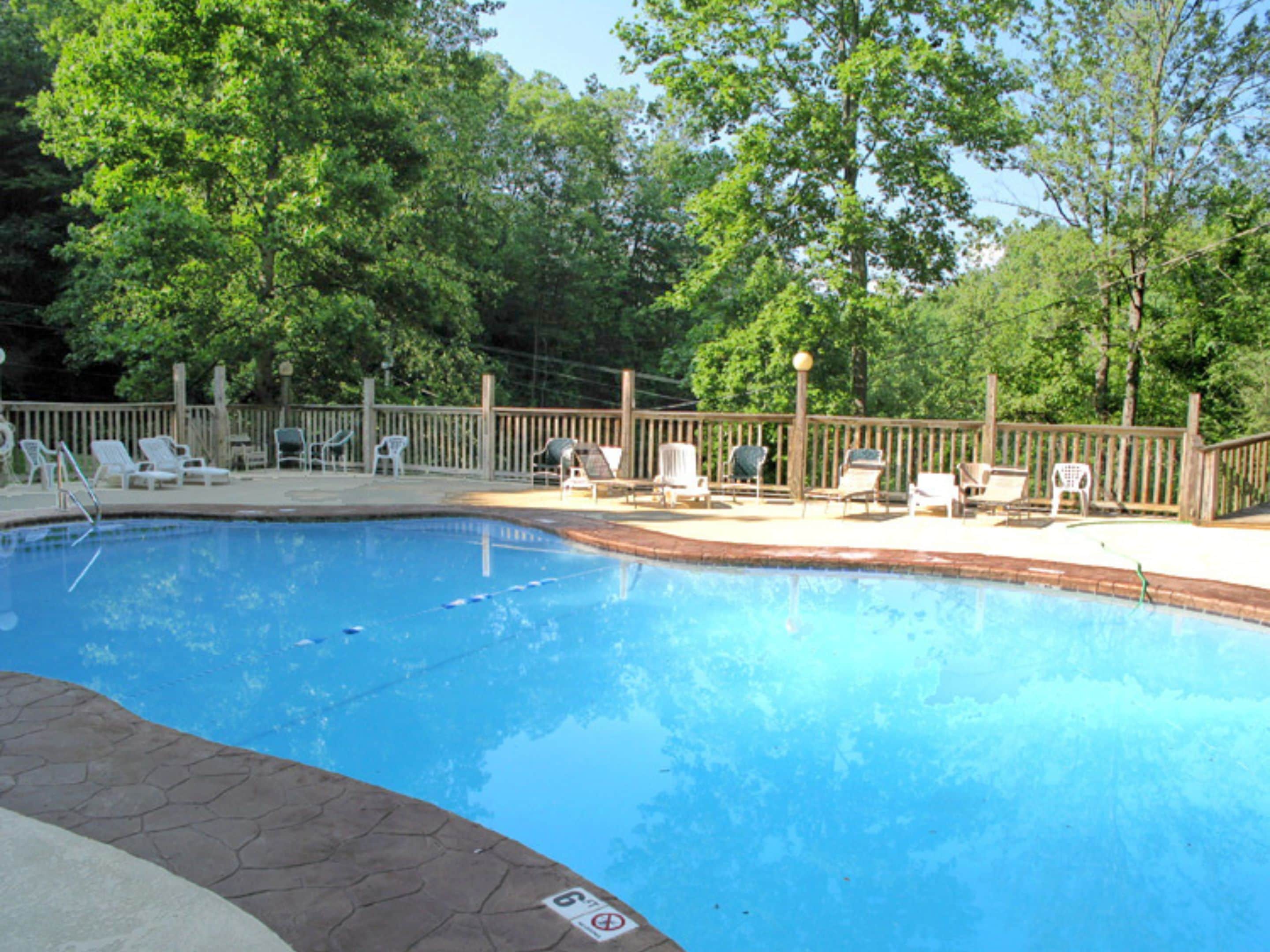 A swimming pool with a wooden deck, surrounded by trees and equipped with lounge chairs.
