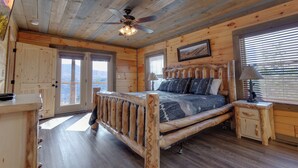 A wooden cabin bedroom with a bed, a nightstand, a ceiling fan, and a window with blinds. - Great Smoky Lodge by Jackson Mountain Rentals (Gatlinburg)