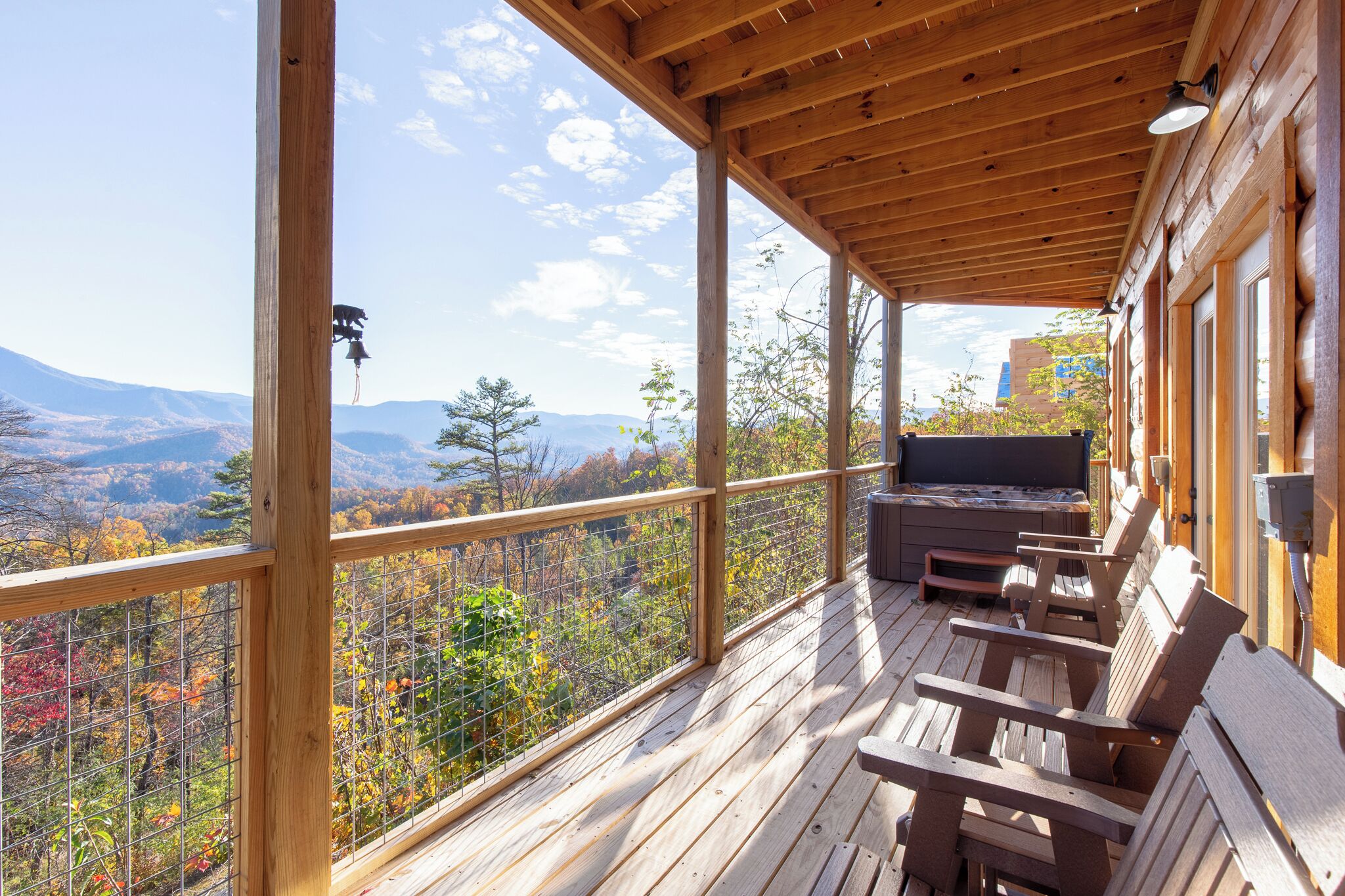 A wooden deck with a view of mountains and autumn foliage, outdoor seating, and a fireplace.