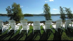 Weiße Adirondack-Stühle, die auf einen See mit blauem Himmel blicken.