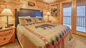 Une chambre confortable, aménagée dans le style d’un chalet, avec une tête de lit en bois, un lit recouvert d’une couette à motifs d’ours, deux lampes de chevet et un ventilateur de plafond.