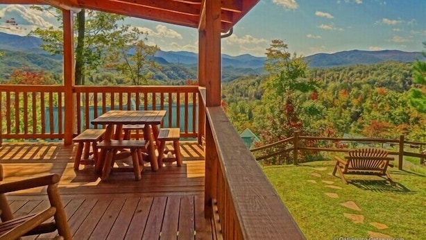 Une terrasse en bois avec des tables de pique-nique et un banc, offrant une vue sur un paysage montagneux.
