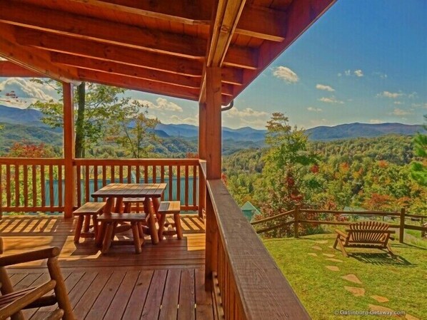 A wooden deck with picnic tables and a bench, overlooking a mountainous landscape.