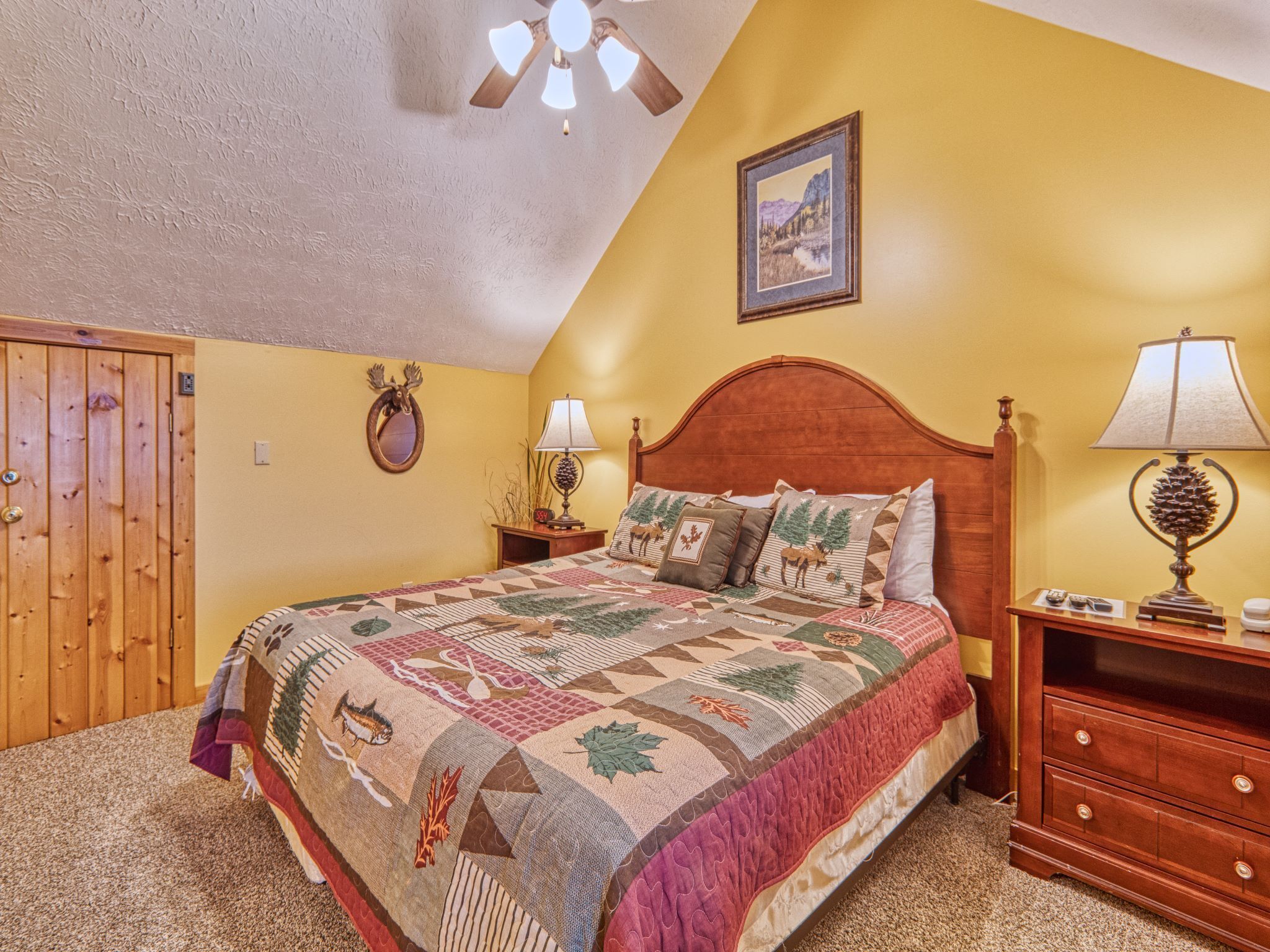 A bedroom with a wooden bed, a ceiling fan, a wooden wardrobe, and a painting on the wall.