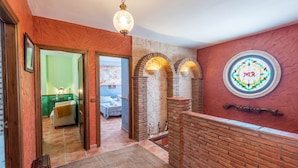 Een hal met een bakstenen muur, een rond glas-in-loodraam en een deur naar een kamer met een bed en een groene muur.