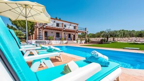 Ein Poolbereich mit Liegestühlen und einem großen Sonnenschirm, ein Schwimmbecken und ein Gebäude mit Balkon im Hintergrund.