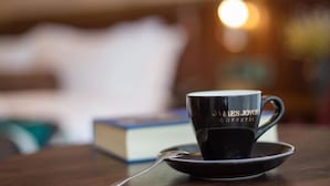 A black coffee cup with "James Joyce Coffee" text on a saucer, placed on a wooden table with a blurred background including a book and a lamp. - James Joyce Coffetel (Zunyi Bozhou Nanbai) (Zunyi)