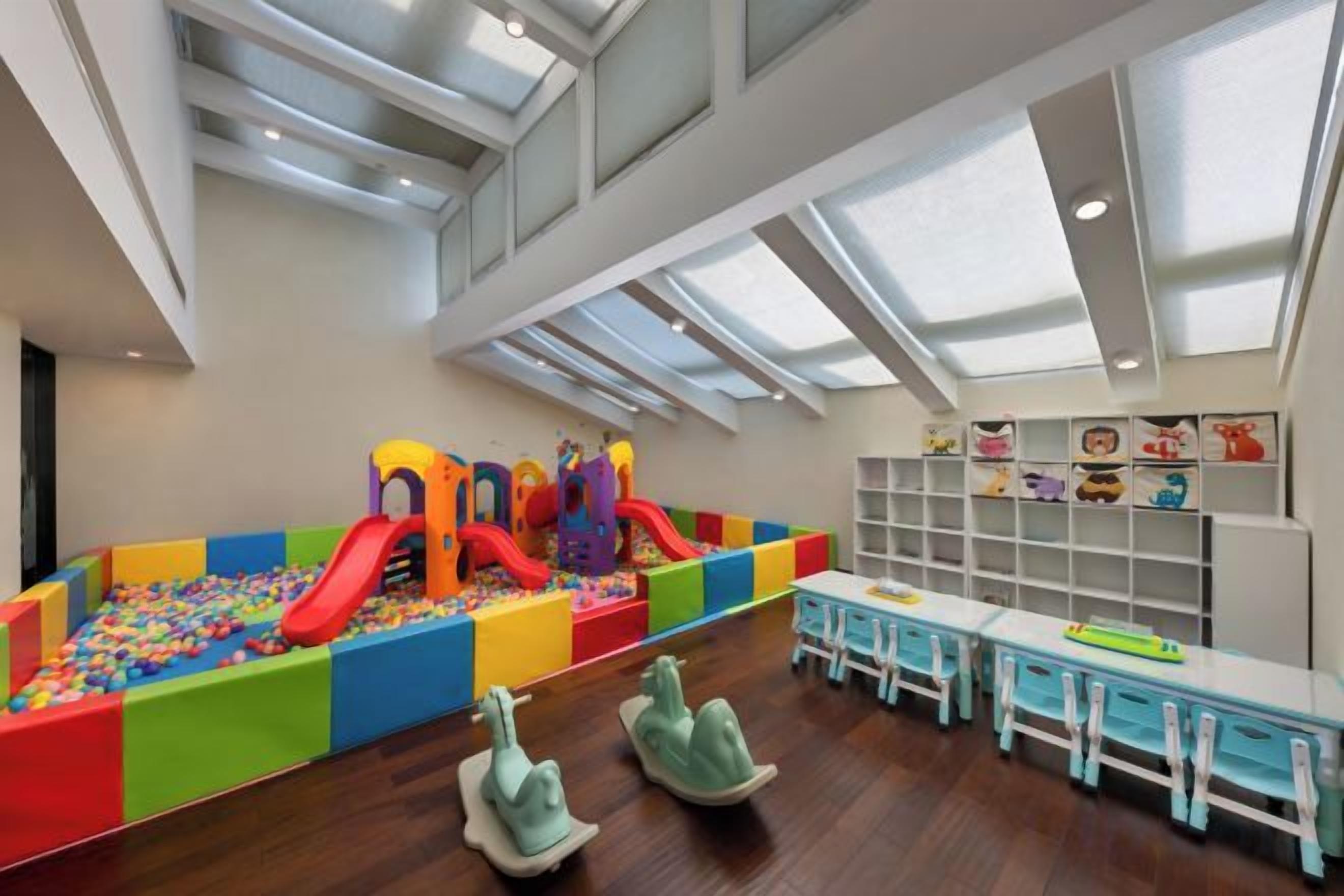 A play area with slides and a ball pit, surrounded by tables and chairs.