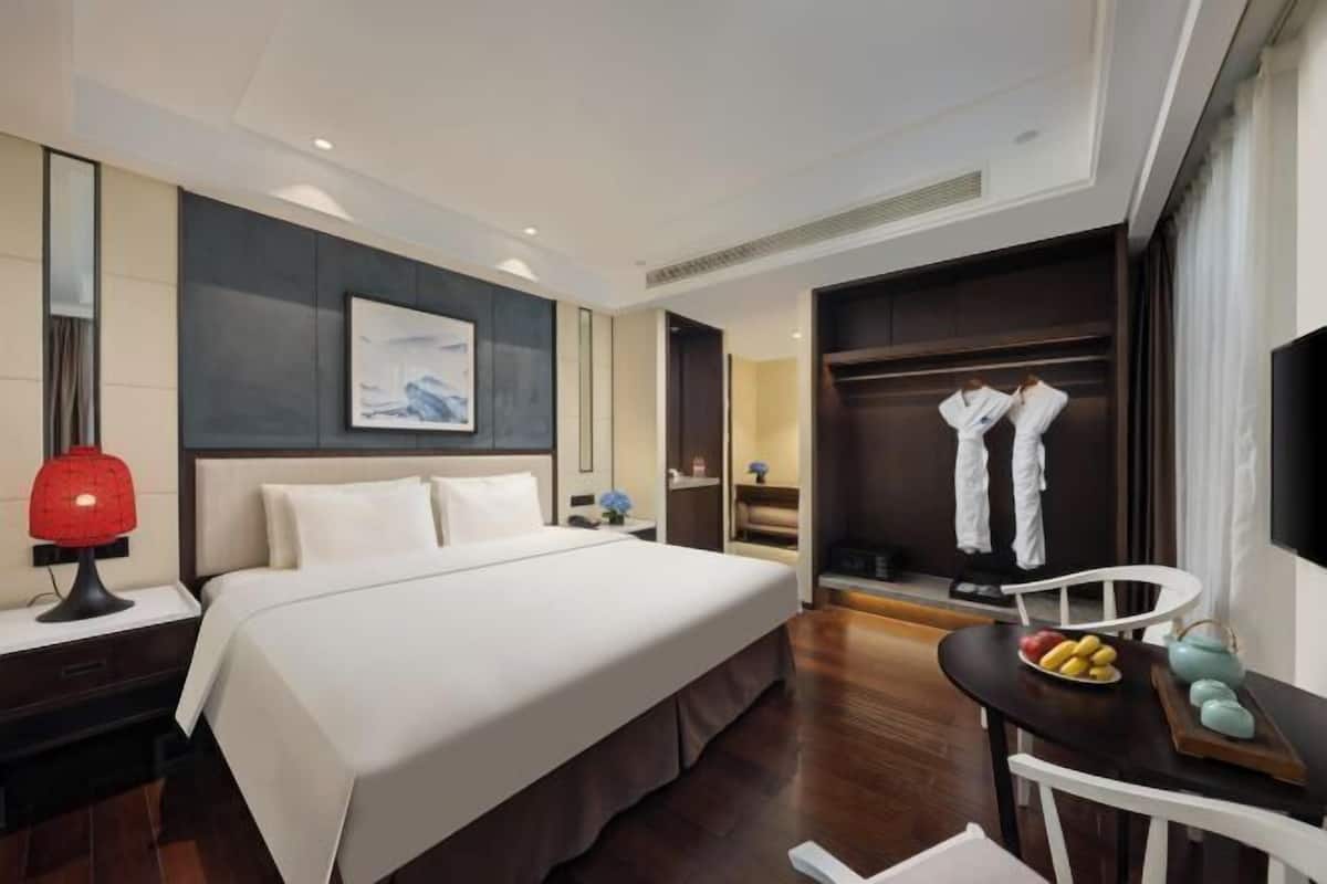 Ein Hotelzimmer mit einem Bett, einem Nachttisch mit Lampe, einem kleinen Tisch mit Obst, einem Sessel und einem Kleiderschrank.