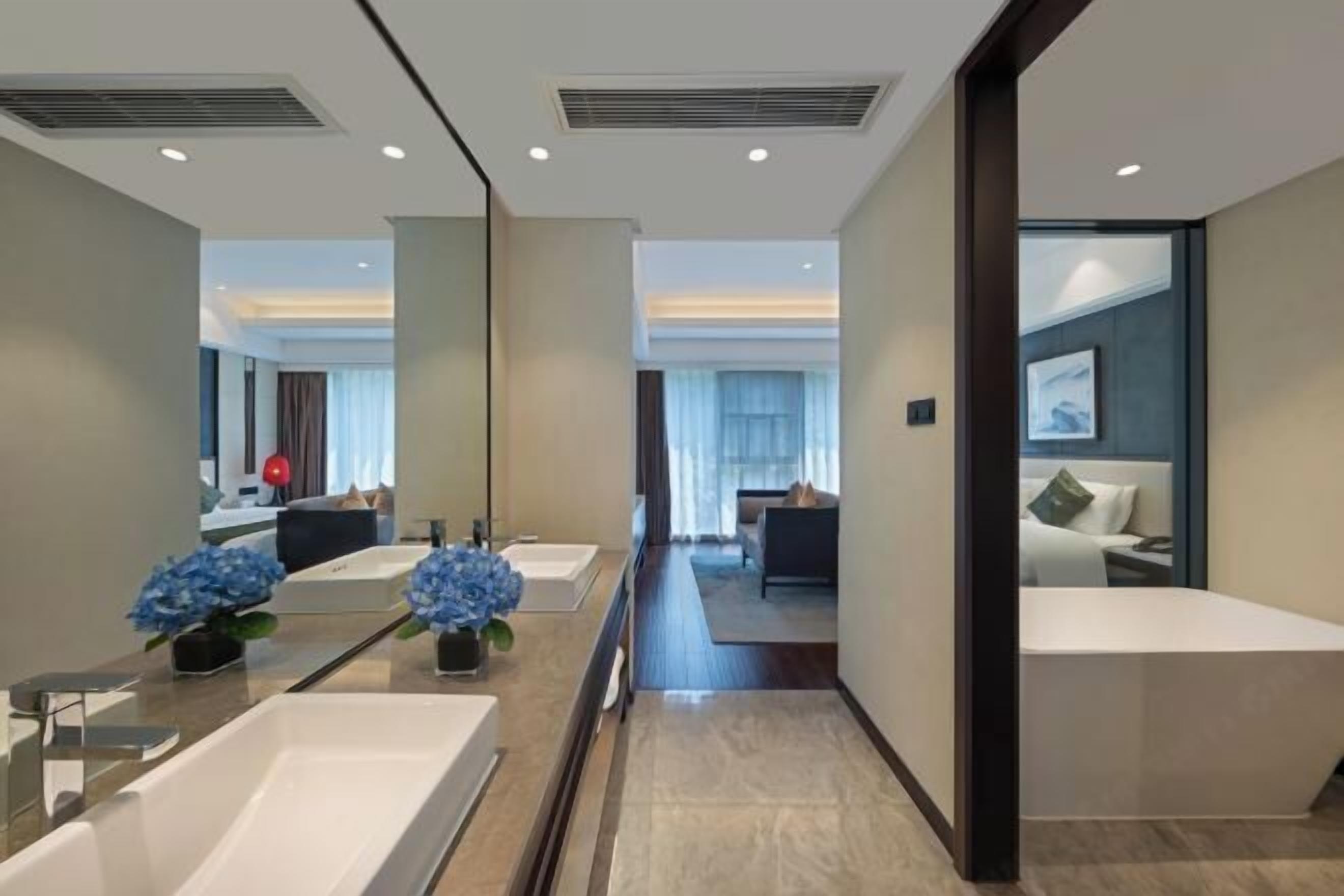 A modern hotel bathroom with a large mirror, two sinks, and a shower area.