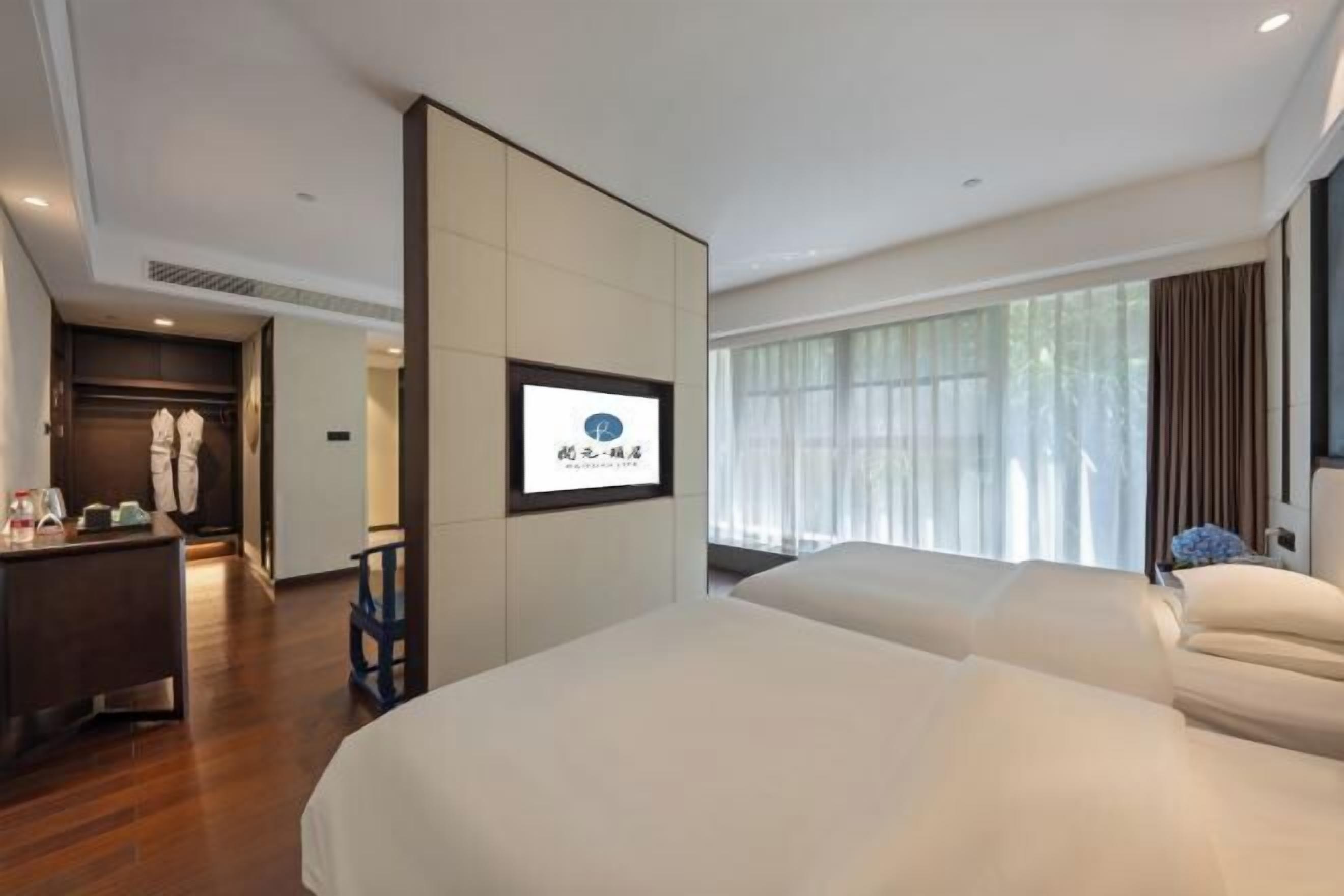 A hotel room with two beds, a desk, and a large window with curtains.