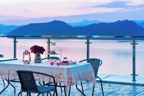 Una mesa para dos con sillas, mantel y vista a un lago y montañas.
