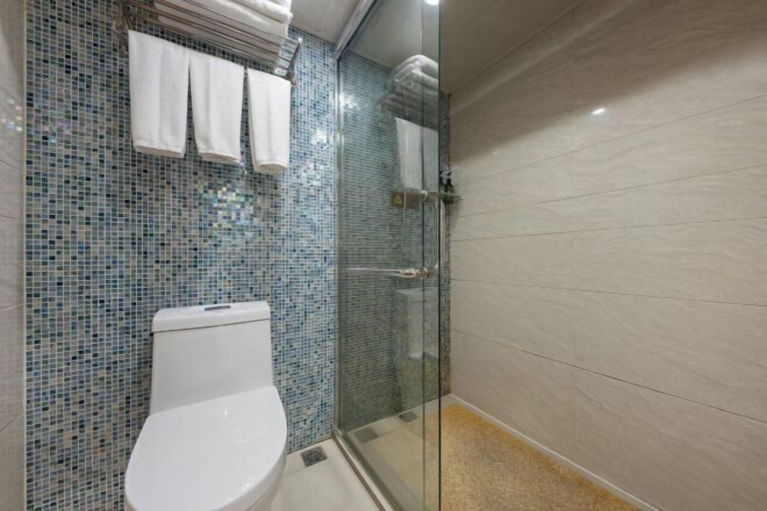 Un baño con inodoro, ducha con puerta de cristal y pared de azulejos.