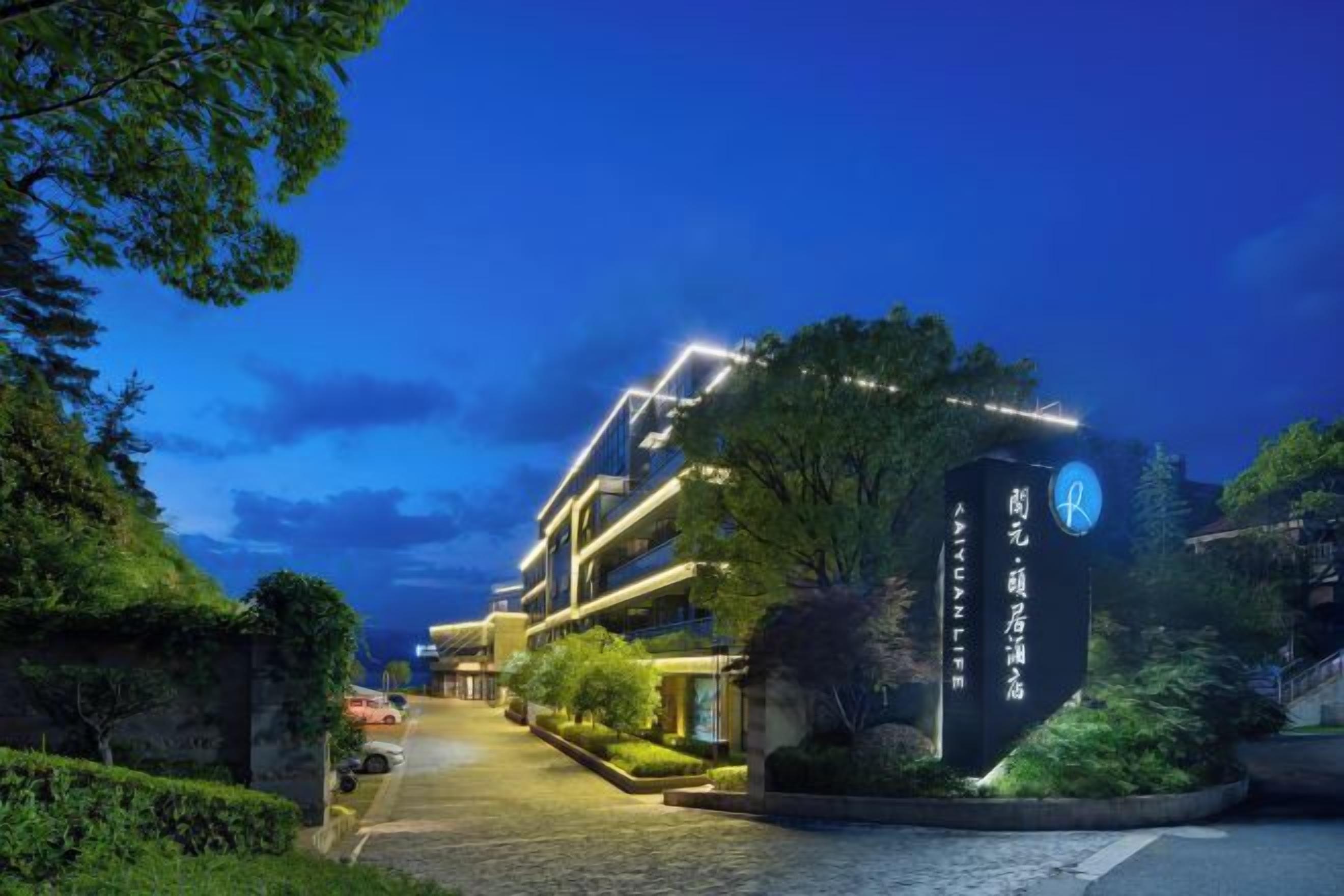 Un hotel moderno con una entrada bien iluminada, un letrero con escritura extranjera y un camino ajardinado que conduce al edificio.