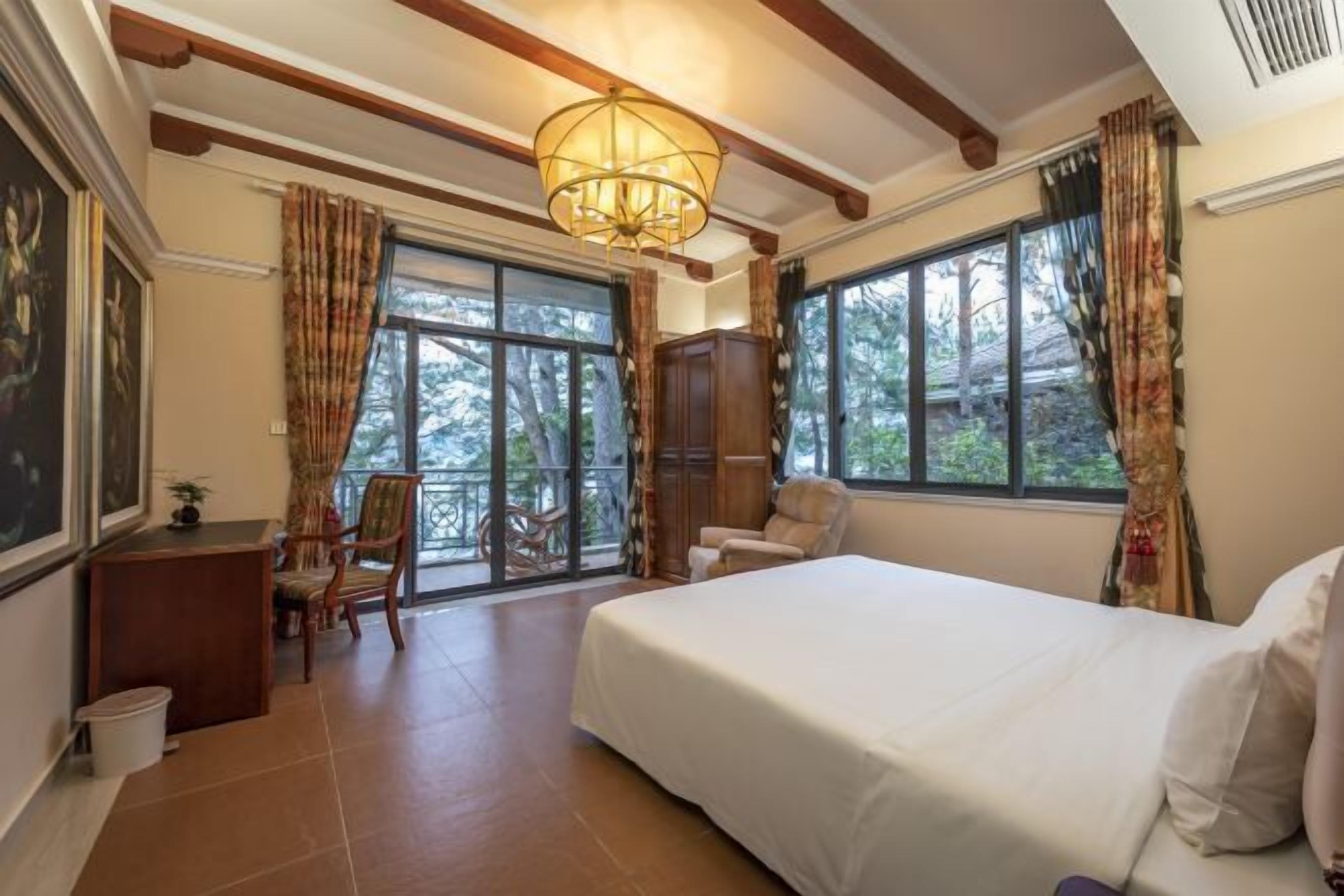 A bedroom with a large bed, a desk, a chair, and a window with curtains.