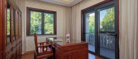 A room with a wooden desk, a chair, a cabinet, and a large sliding glass door leading to a balcony.