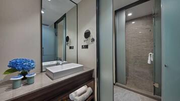 Une salle de bain moderne avec un grand miroir, un lavabo blanc et une douche à parois de verre.