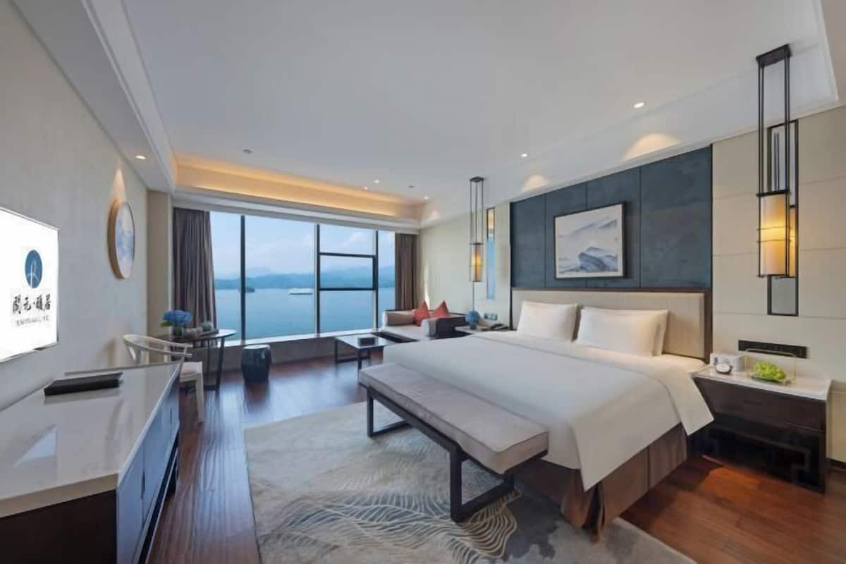 Ein modernes Hotelzimmer mit einem großen Bett, einem Schreibtisch, einer Bank und Blick aufs Meer.
