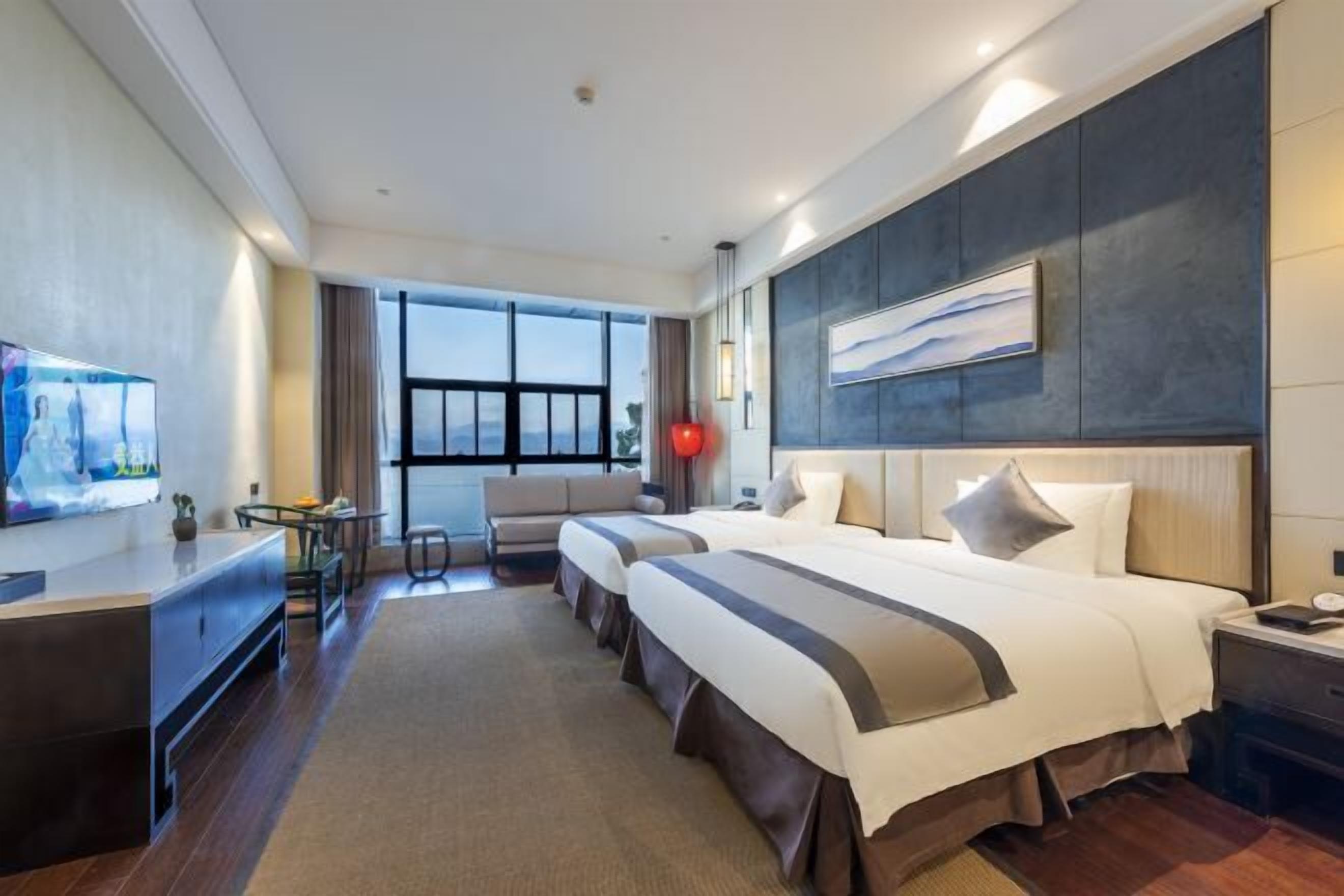 A hotel room with two beds, a desk, a TV, and a large window.