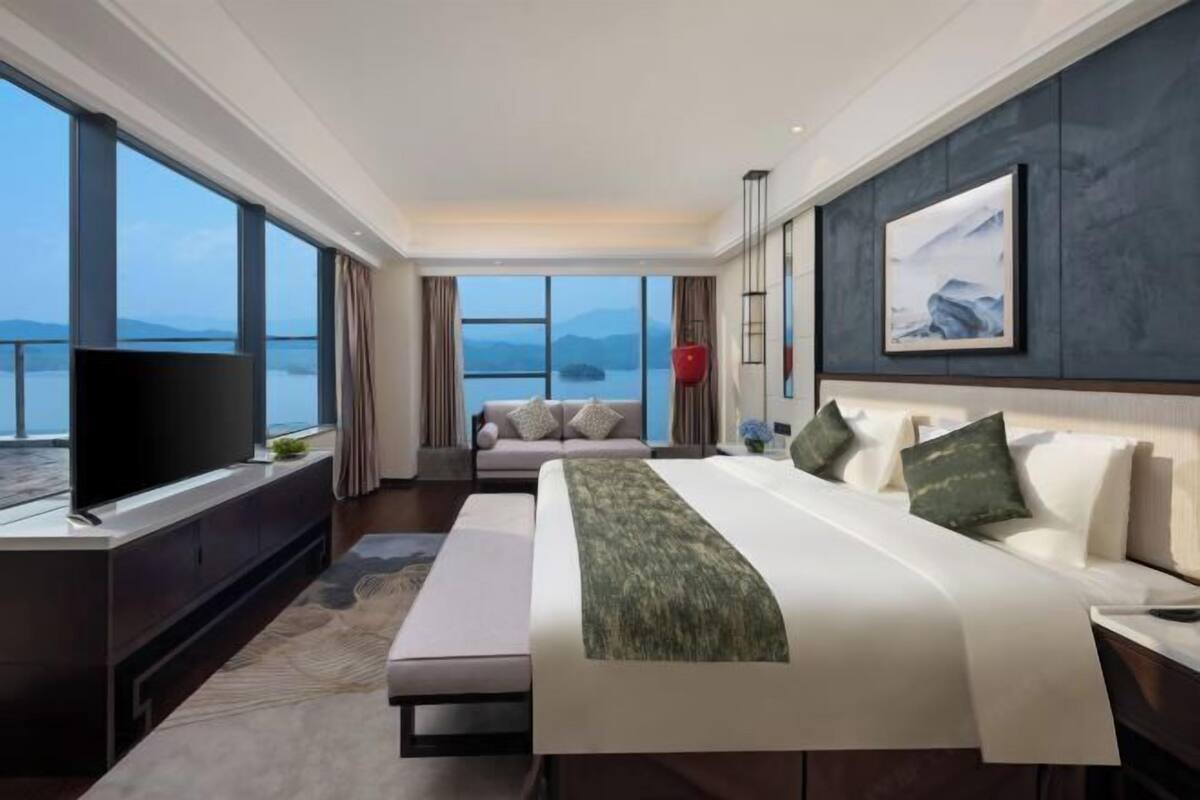 Ein modernes Hotelzimmer mit einem großen Bett, einem Fernseher, einer Couch und Blick auf das Wasser.