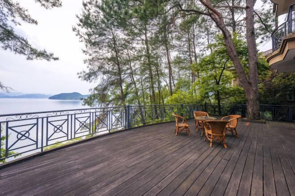 Eine Holzterrasse mit Gartenmöbeln, die auf ein Gewässer blickt und von Bäumen umgeben ist.