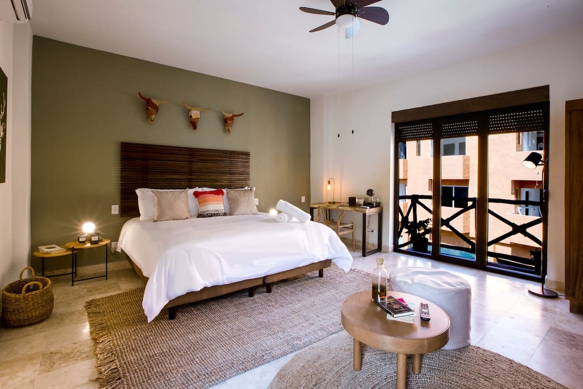 A well-lit bedroom with a large bed, bedside tables, a ceiling fan, and a view through a glass door to an outdoor area.