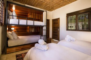 Ein Zimmer mit zwei Betten, darunter einem Schlafmaßbett, Holzwänden, einer gewebten Decke und einem Fenster mit Jalousien.