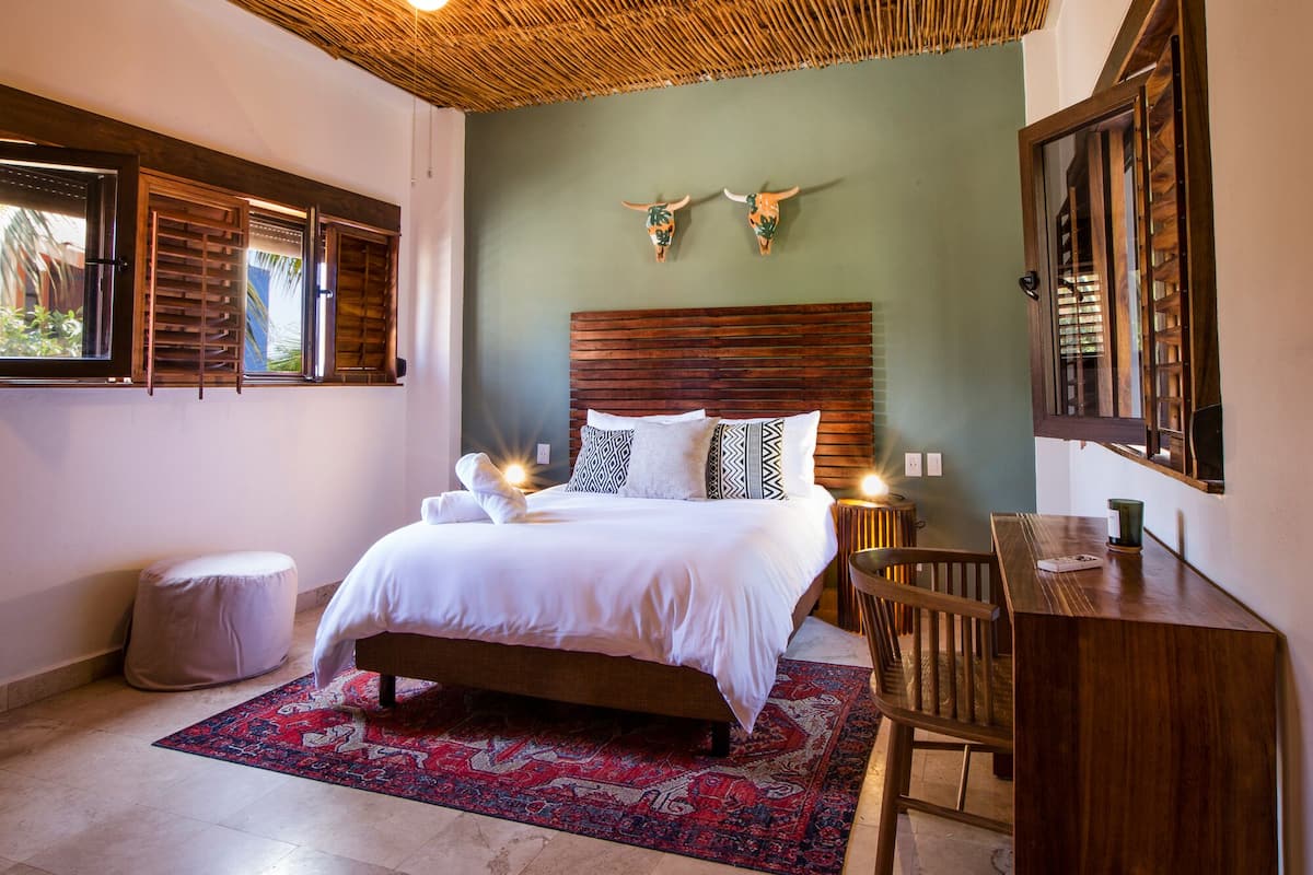A bedroom with a bed, a desk, a chair, a rug, and decorative wall art.