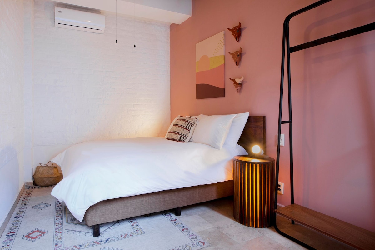 A bedroom with a bed, a bedside lamp, a wall-mounted air conditioner, and a small rug.