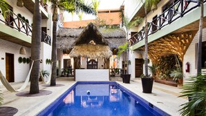 A pool area with a thatched-roof structure, palm trees, and a white building with balconies. - Selina Sayulita (Sayulita)