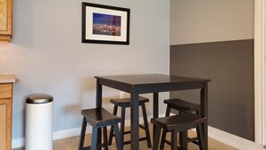 Un pequeño comedor con una mesa de madera oscura y tres taburetes a juego. Encima de la mesa, cuelga un cuadro enmarcado.