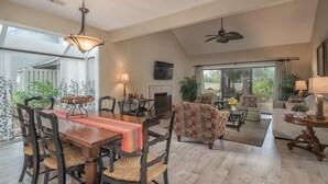 A spacious living area with a dining table, chairs, a sofa, and a TV mounted on the wall.