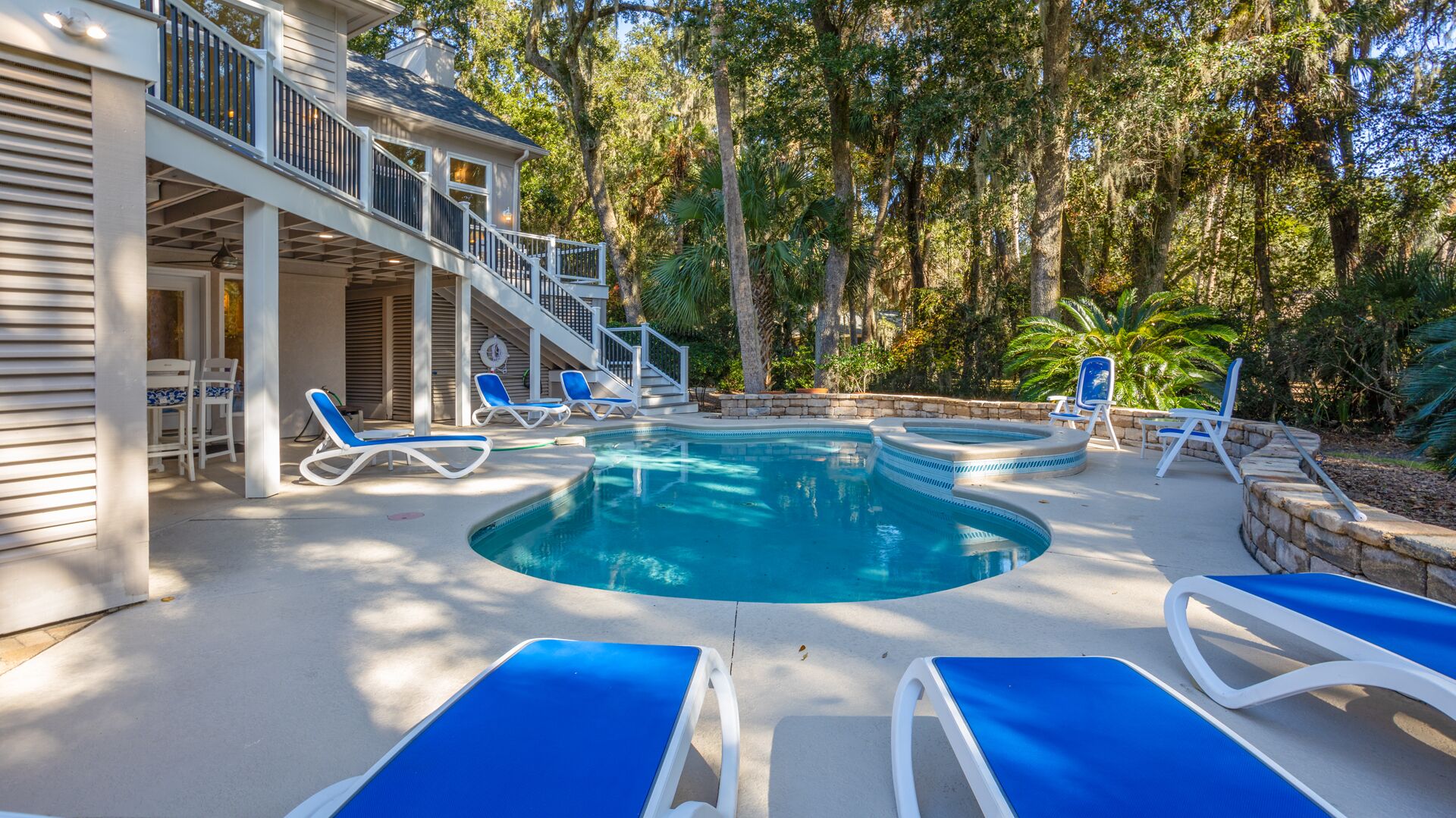 Uma área de piscina com cadeiras de descanso, uma banheira de hidromassagem e uma escadaria que leva a um deck coberto.