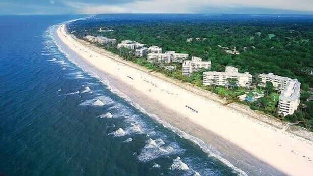 An aerial view of a coastal area with a sandy beach and a row of buildings along the shore.
