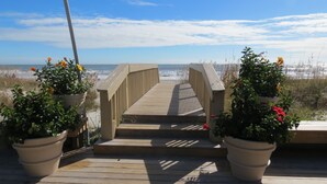 A wooden boardwalk leading to the beach with potted plants on either side.
