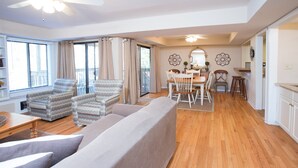 A spacious living area with a large sofa, patterned armchairs, a dining table with chairs, and a kitchen area with cabinets and a countertop.