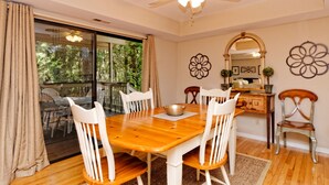 A dining area with a wooden table and white chairs, a ceiling fan, and a view through a glass door to an outdoor deck.