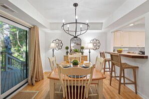 A dining area with a chandelier, wooden table, chairs, and a view of a balcony.
