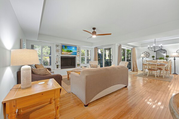 A spacious living area with a fireplace, a dining table, and a ceiling fan.