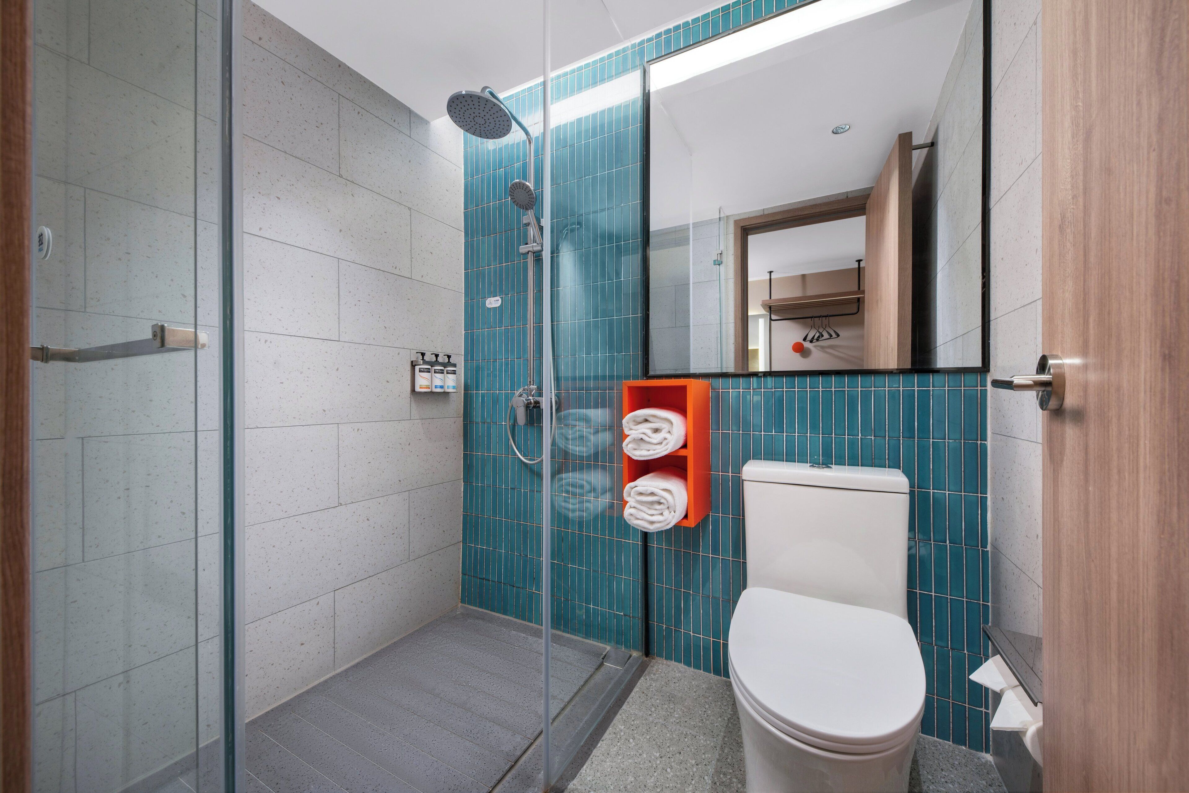 A modern bathroom with a glass shower enclosure, a toilet, and a towel rack with folded towels.