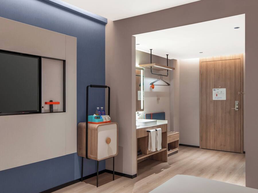 A modern hotel room with a large mirror, a wooden cabinet, a sink, and a wardrobe.